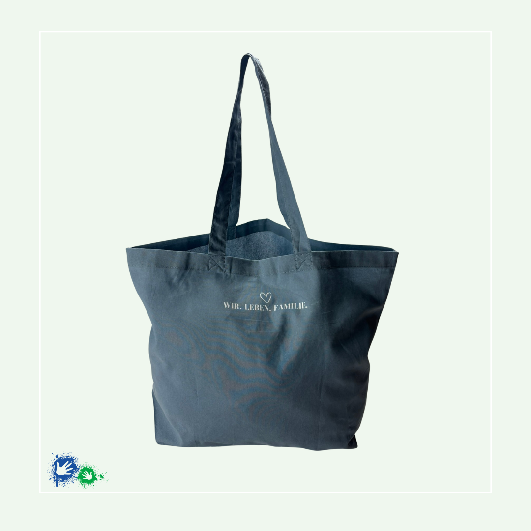 Einkaufstasche in der Farbe "Dusty Blue" (blau) von hinten mit dem weißen Schriftzug: WIR. LEBEN. FAMILIE., darüber ein Herz.