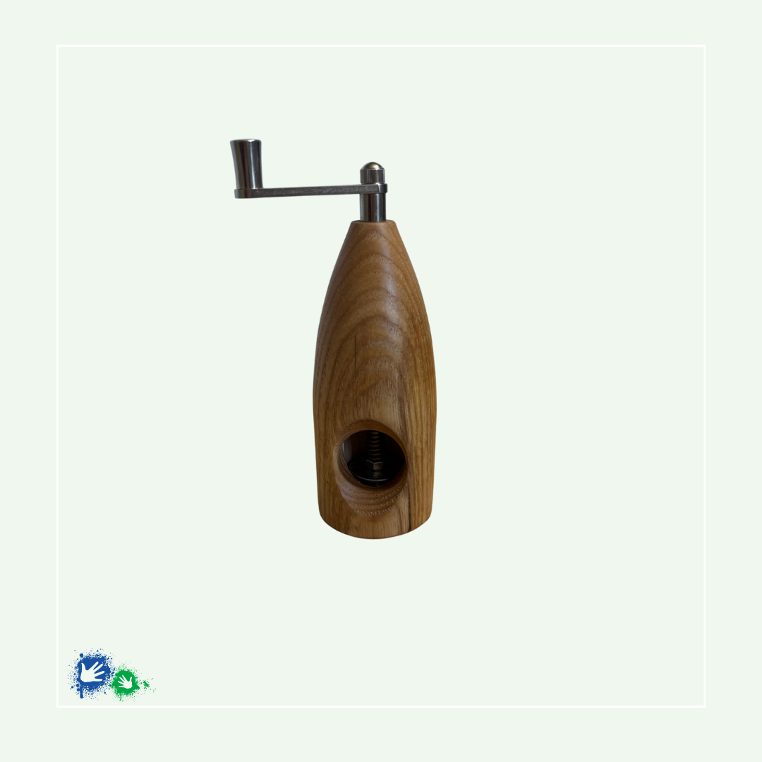 Eine Muskatmühle aus mittelbraunem Holz mit einer Kurbel oben. Das Bild zeigt die Mühle von der anderen Seite mit dem Loch, in das die Muskatnuss eingelegt und in das Mahlwerk eingeklemmt wird.