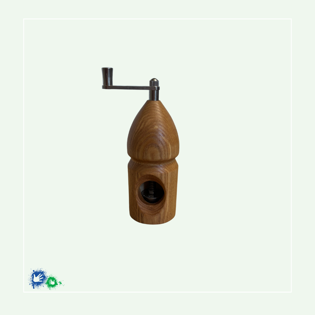 Eine Muskatmühle aus mittelbraunem Holz mit einer Kurbel oben. Das Bild zeigt die Mühle von der anderen Seite mit dem Loch, in das die Muskatnuss eingelegt und in das Mahlwerk eingeklemmt wird.