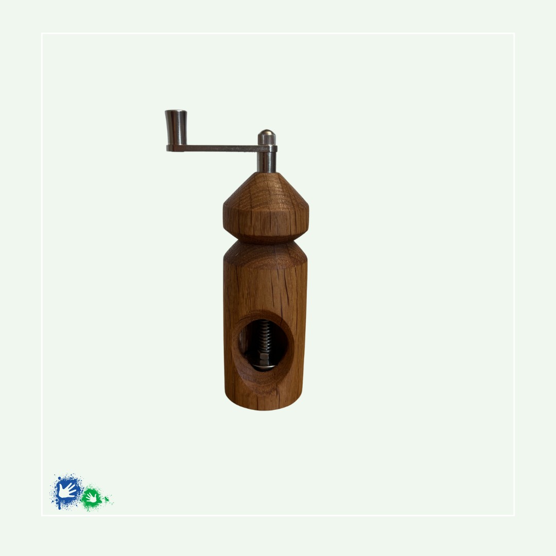 Eine Muskatmühle aus mittelbraunem Holz mit einer Kurbel oben. Das Bild zeigt die Mühle von der anderen Seite mit dem Loch, in das die Muskatnuss eingelegt und in das Mahlwerk eingeklemmt wird.