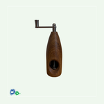 Eine Muskatmühle aus dunklem Holz mit einer Kurbel oben. Das Bild zeigt die Mühle von der anderen Seite mit dem Loch, in das die Muskatnuss eingelegt und in das Mahlwerk eingeklemmt wird.