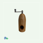 Eine Muskatmühle aus mittelbraunem Holz mit einer Kurbel oben. Das Bild zeigt die Mühle von der anderen Seite mit dem Loch, in das die Muskatnuss eingelegt und in das Mahlwerk eingeklemmt wird.