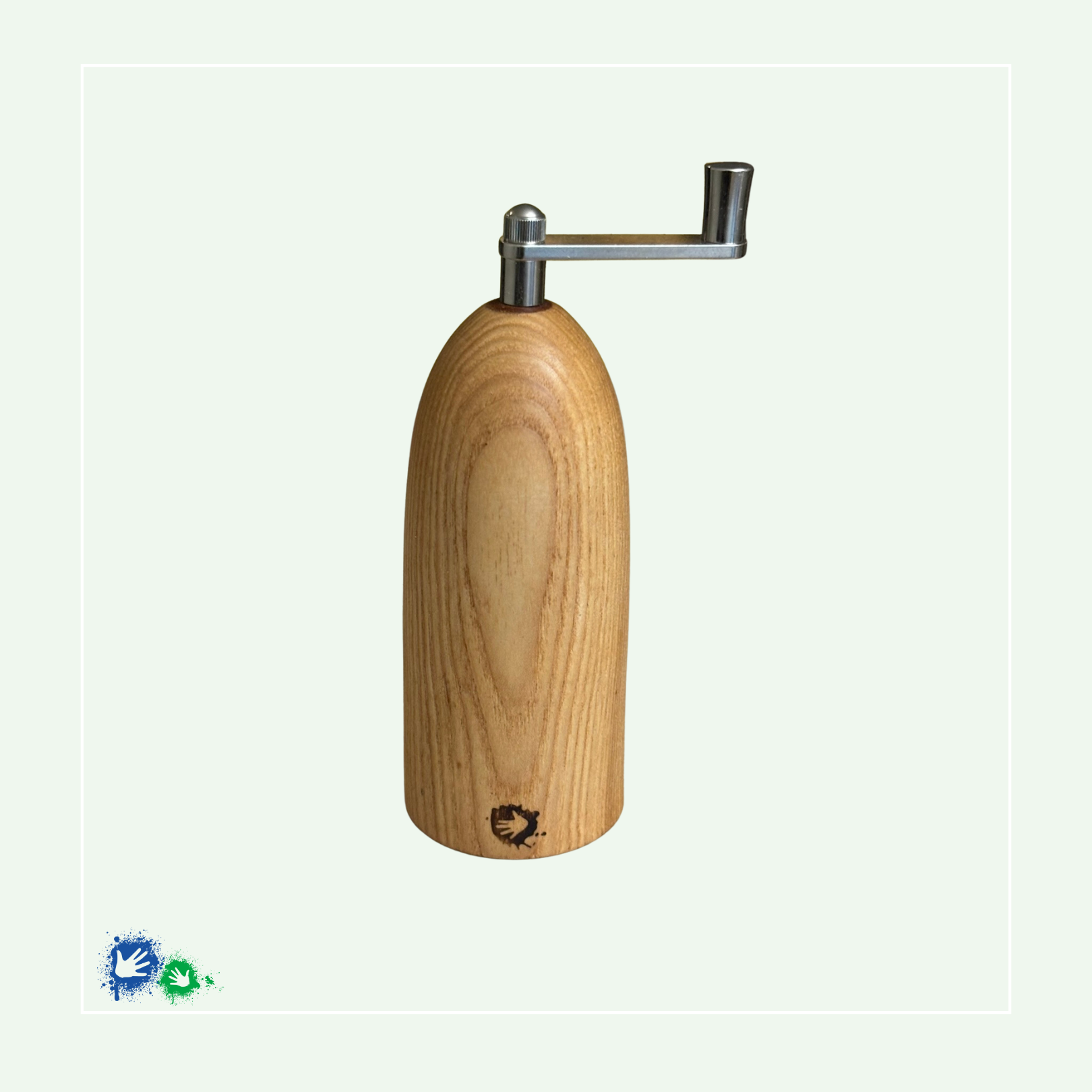 Eine Muskatmühle aus hellem Holz mit einer Kurbel oben. Unten ist ein Hände-Logo eingebrannt.