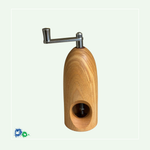 Eine Muskatmühle aus hellem Holz mit einer Kurbel oben. Das Bild zeigt die Mühle von der anderen Seite mit dem Loch, in das die Muskatnuss eingelegt und in das Mahlwerk eingeklemmt wird.